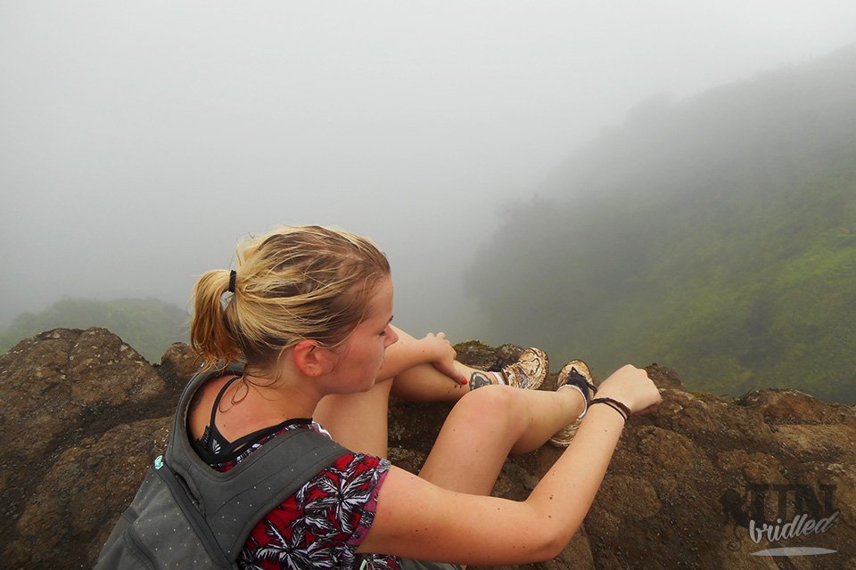 Blonde Frau sitzend am Rande des Kuliouou Gipfels, umgeben von einer dicken Wolke, die nichts von der Aussicht erahnen lässt