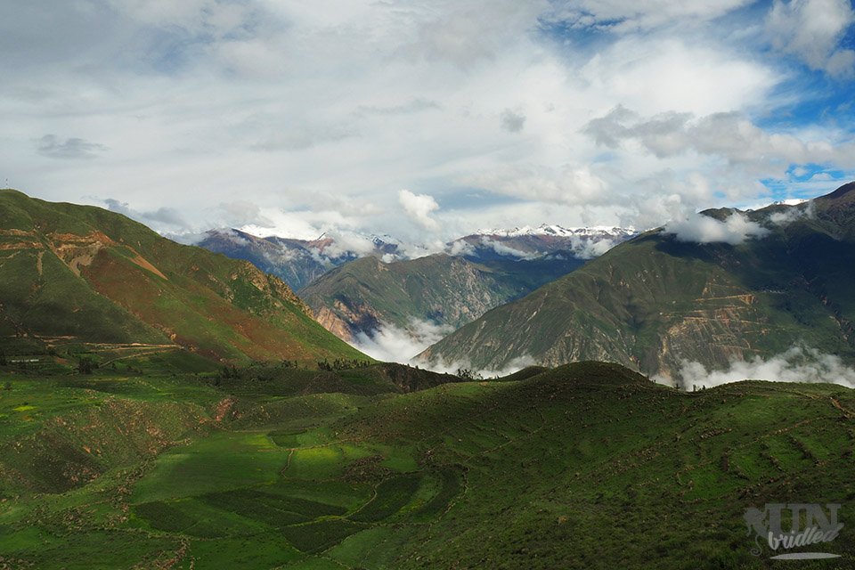 A green field on the side of the trail to Llahuar, clouds fill the valley with mountains in the background