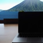 Laptop auf einem Tisch mit Panoramasicht aus dem Fenster und dem Text: Atitlan-See - Digitale Nomaden Guide
